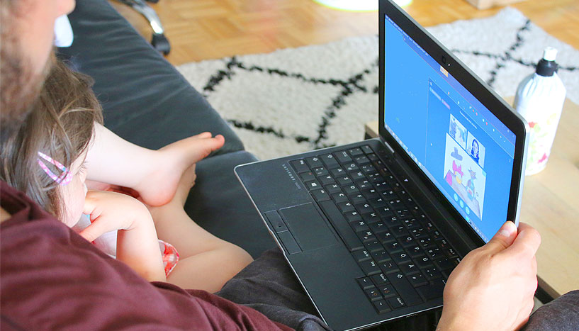 Mann mit Kind im Arm vor einem Laptop sitzend.