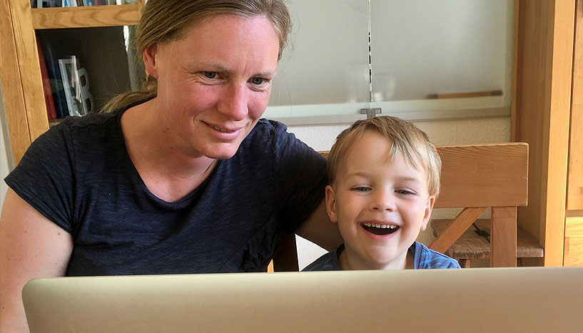 Frau mit Kind vor Laptop sitzend.